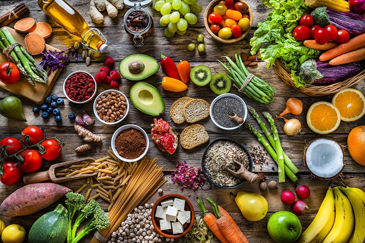 Vegan food backgrounds: large group of fruits, vegetables, cereals and spices shot from above Vegan food backgrounds: large group of multicolored fresh fruits, vegetables, cereals and spices shot from above on wooden background. The composition includes green apple, kiwi, pear, pomegranate, orange, coconut, banana, grape, berries, ginger, almonds, pistachio, olive oil, olives, goji berries, chia seeds, pinto beans, nutmeg, rosemary, radish, tomatoes, carrot, kale, avocado, onion, rice, cocoa powder, sweet potato, wholegrain pasta, tofu, lettuce, corn, broccoli, pepper, asparagus, green beans, among others. High resolution 42Mp studio digital capture taken with SONY A7rII and Zeiss Batis 40mm F2.0 CF lens